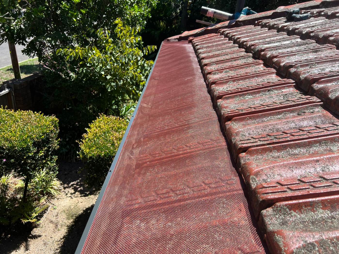 Red tile roof with dark gutter guard mesh fitted along the gutter line