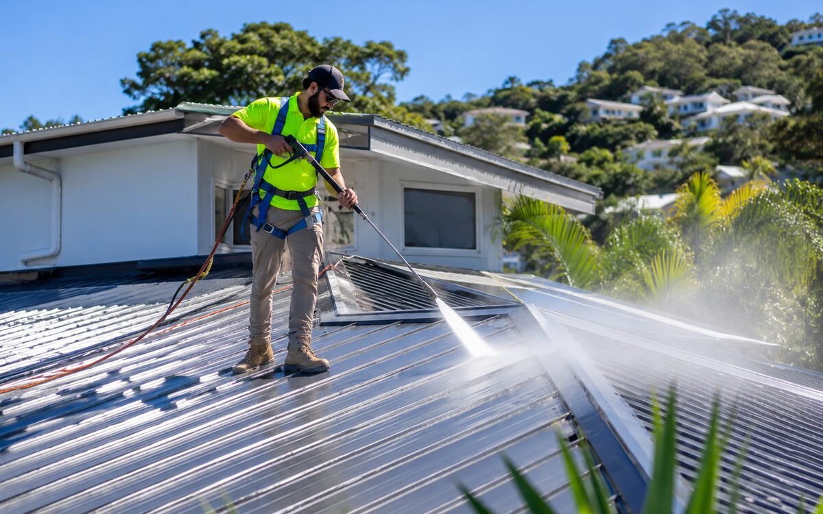 Technician in harness pressure washing a metal roof